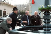 Bürgermeister Schattenhofer hofft auf einen Zeitungsartikel über den Lansinger Wunschbrunnen und wirft hierfür Münzen in den Brunnen. Von links: Xaver (Michael Schreiner), Lorenz Schattenhofer (Werner Rom), Pfarrer Kurz (Hans Stadlbauer) und Martin Kirchleitner (Hermann Giefer).