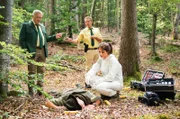 Hubert (Christian Tramitz, M.) und Girwidz (Michael Brandner, l.) versuchen der Pathologin Dr. Caroline Fuchs (Susu Padotzke, r.) zu erklären, wie sie auf die Leiche des Försters Ulf Gröschel (Komparse) gestoßen sind.