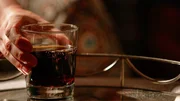 Eine Hand hält ein Glas auf dem Tisch
