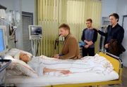 Betroffen und sprachlos stehen Jan (Timothy Peach, r.), Sönke (Bo Hansen, 2.v.l.) und Robin (Niklas Osterloh, l.) an Claudias (Mignon Remè, l.) Krankenbett.