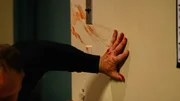 Ein Mann klammert sich mit einer blutigen Hand an die Wand