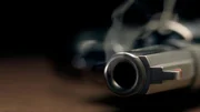 A gritty crime scene image of a smoking hand gun, revolver, lying on the floor with narrow focus on the tip if the barrel and dark background