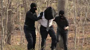 Eco-terrorists lead a hooded Sidney through the woods at gun point