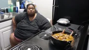 Kelly sitting in front of a stove cooking.
