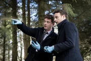 DI Archie Dent (Josh Bolt, l.) macht Harper (Andrew Gower, r.) mit den Lokalitäten des neuen Falls vertraut.