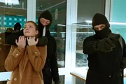 Die Mitarbeiterin Leonie Seidel (Valerie Sophie Körfer, l.) wird als Geisel genommen, als zwei maskierte Alexander Brösser (Vincent Krüger, M.) und Mike Holland (Nico Ehrenteit, r.) den Juwelier Feith überfallen.