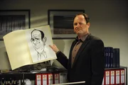 Hubert (Bernhard Ulrich) sucht nach einem geeigneten Platz, um seine Karikatur vor Martin zu verstecken.