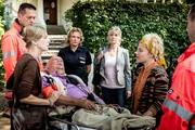 Friedrich Magnus (Christian Grashof, liegend) hat der Besuch seiner Tochter Constanze (Milena Dreißig, l.) und deren Anschuldigungen, dass die Musikstudentin Paula Tennhagen (Charly Ann Schmutzler, 2.v.r.) ihn wegen seines Geldes und Hauses ausnutzen würde, derart aufgeregt, dass er einen Zusammenbruch erlitten hat. Claudia (Janette Rauch, 4.v.l.) und die Sozialarbeiterin Karin Berger (Anne Kasprik, 3.v.r.) sind unschlüssig, was sie von der ganzen Situation halten sollen.