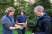 Die Frauen wissen sich zu helfen! Beatrice (Mitte) und Andrea (rechts) behandeln Giselas allergischen Ausschlag an den Armen mit Spitzwegerich.