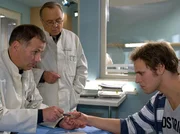 Dr. Roland Heilmann (Thomas Rühmann, links) und Prof. Simoni (Dieter Bellmann, Mitte) untersuchen den verletzten Daumen von René Beek (Michael Schumacher). Die Verletzung ist so schwer, dass der Daumen wahrscheinlich amputiert werden muss. Für René wäre das eine Katastrophe. Er sitzt im Rollstuhl und braucht seine Daumen und auch Basketballspielen könnte er dann nicht mehr.