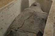 The mummy of the priest Ayput. The name indicates that he is male but beneath the dark outer layer and the linen wrappings, slight bulges can be seen, especially on the mummy's upper left side. This is indicative of the priest's left arm being crossed over the chest - a position usually reserved for women. It raises questions for Ramadan and the team - could this priest be a priestess? (National Geographic/Piers Leigh)