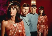 Dr. McCoy (DeForest Kelley, 2.v.l.) und Mr. Spock (Leonard Nimoy, 2.v.r.) beobachten leicht abgestoßen die fremde Welt von Harry Mudd. Der Herrscher hat sich eine Bevölkerung aus Androiden geschaffen, über die er verfügen kann. Die Roboter-Frauen (Darstellerinnen unbekannt) gleichen einander wie ein Ei dem anderen.