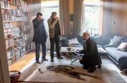 Die Kommissare Finn (Sven Martinek, l.) und Lars (Ingo Naujoks, 2.v.l.) stehen am Fundort der Leiche von Hans Vonnsen. Auf dem Teppich vor ihnen ist ein dunkler Abdruck des bereits stark verwesten Körpers zu sehen. Dr. Henning Strahl (Christoph Tomanek, r.) kniet auf dem Boden und dokumentiert den Tatort mit seiner Kamera.
