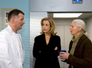 Dr. Roland Heilmann (Thomas Rühmann, li.) muss Gerda Freitag (Solveig Müller, re.) sagen, dass es bei der OP ihres Mannes Komplikationen gegeben hat. Gerda bereut sofort, ihren Mann zur OP geraten zu haben. Als Sarah Marquardt (Alexa Maria Surholt, mi.) dieses Gespräch mitbekommt, bleibt sie stehen und hört mit.