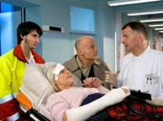 Gerda Freitag (Solveig Müller, liegend) wird vom Notarzt (Roman Petermann, links) und von ihrem Mann Alfred (Volkmar Kleinert, Mitte) in die Sachsenklinik gebracht. Als sie dort von Dr. Roland Heilmann (Thomas Rühmann) aufgenommen werden, besteht Alfred Freitag darauf, seine Frau zu den Untersuchungen zu begleiten.