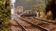 Ein Renault Espace, der auf einer Eisenbahnlinie mit entgegenkommendem Zug geparkt ist.