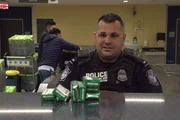 Officer Graham sitzt an seinem Schreibtisch und recherchiert, was das Medikament vor ihm ist. (National Geographic/Lucky 8 TV)