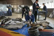 RE-CREATION:  Tom Haueter (played by Danny Deakin) picks up a piece of debris while other investigators (played by background performers) look at other pieces from the wreckage.   (photo credit:  Cineflix/Ian Watson)