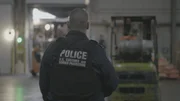Officer stands by while workers move shipment at warehouse facility. (National Geographic)