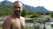 Ed Stafford standing by a body of water in Patagonia in a mountainous region.