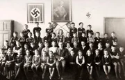 Ein Klassenporträt von jungen Schulkindern mit ihrem Lehrer vor einer Fotografie von Adolf Hitler und zwei Hakenkreuzen während des Zweiten Weltkriegs, um 1940.