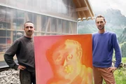 Florian Maritz präsentiert «Kulturplatz»-Host Nino Gadient (rechts) sein gemaltes Kunstwerk auf der Alp Gitschenen vor einer Bergkulisse.
