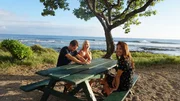 Home buyers Rachael Adair (M), Dan Adair (L) and Realtor Rebecca Morton (R) sitting at a picnic table by the ocean as seen on Hawaii Hunters (Action) Home buyers Rachael Adair (M), Dan Adair (L) and Realtor Rebecca Morton (R) sitting at a picnic table by the ocean as seen on Hawaii Hunters (Action)
