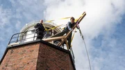"Hab ihn!" - Mit Fingerspitzen greift Hinnerk Feldmann (Oliver Wnuk, r.) den geborstenen Karabinerhaken, der Stefan Conrad beim tödlichen Sturz zum Verhängnis geworden ist. In luftiger Höhe auf der Seilwinde wird er durch einen Polizisten (Komparse) gesichert.