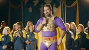 In der finalen Runde gibt Thunderbolt (Olli Wermskog, Mitte) vor den applaudierenden Schüler*innen den Gewinner von SuperDupers Wettbewerb bekannt.