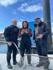 Ross Kemp (links), der Meeresarchäologe Mallory Haas und der Tauchleiter (rechts) Neil Brock halten die kupferne Rumpfscheide in der Hand, die sie am Standort des Kriegsschiffs HMS Amethyst von 1799 geborgen haben. Plymout