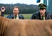 Hubert (Christian Tramitz, links) und Staller (Helmfried von Lüttichau) versuchen die Kuh von der Straße zu bewegen - ohne Erfolg! Dann setzt Hubert einen Warnschuss in die Luft ab und die Kuh trottet langsam von der Straße ab.