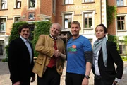 Hotelier Peter Herbrechter (Michael König, 2.v.l.) schüttelt Andreas Marthaler (Martin Gruber, 2.v.r.) vor der Presse die Hand. Die Teilhaber des Hotels, Tobias Herbrechter (Markus Brandl, l.) und Sarah Kraus (Stephanie Stumph, r.), begleiten sie zu diesem Termin.