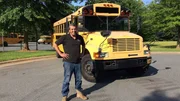 Michael Manousakis standing in front of the yellow school bus.