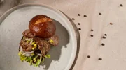 Burger aus kross gebratenen Lammstreifen, Brötchen, Senf und Salat.