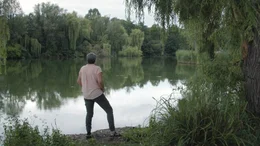 Protagonistin Angelika steht gedankenversunken an einem See.