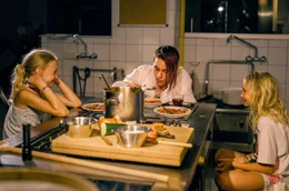 Lotte (Delphine Lohmann, links) bringt ihrer Schwester Luise (Mia Lohmann) Kochgerichte bei. Koch Matteo (Vincent Sauer) hilft ihnen dabei.