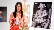 Mai Thi Nguyen-Kim im Studio, umgeben von Fotos von Neugeborenen. Mit Hilfe eines Granatapfels und eines Beckens erklärt sie den Geburtsprozess beim Menschen.