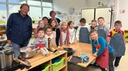 Björn Freitag (l) bereitet gemeinsam mit Lehrerin Malaika Noss (hinten, 2.v.l.) und den Kindern der Koch-AG einfache Kindergerichte zu.