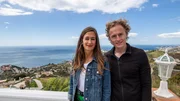 Episode 004 - Holly Prole (L) and Jason Prole (R) standing and smiling, with a view of Mediterranean sea behind them, during their house hunt in the area of La Heradura