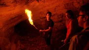 Brasilien: James Fox, Erin Ryder und Ben McGee stehen mit einer Taschenlampe vor einer Höhle. Brasilien: James Fox, Erin Ryder und Ben McGee stehen mit einer Taschenlampe vor einer Höhle.
