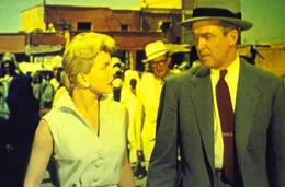 Dr. Ben McKenna (James Stewart, r.) und seine Frau Jo (Doris Day, l.) verbringen ihren Urlaub in Afrika, wo sie bei einer Busreise den mysteri&ouml;sen Louis Bernard treffen. Am n&auml;chsten Tag wird Bernard auf einem Marktplatz get&ouml;tet ...