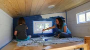 Tiny house owner and builder Sheradan Pate works with her daughter Sage to paint an accent wall in her loft using blue chalkboard paint, as seen on Tiny House, Big Living.