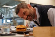 Dr. Mario Herger kostet einen veganen Chickenburger – die Rezeptur wurde entwickelt von einer künstlichen Intelligenz der Firma „NotCo“.