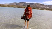 Eine Frau mit einem Rucksack auf dem R&uuml;cken l&auml;uft &uuml;ber das Meer