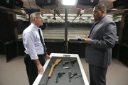 Chris Anderson and Professor Timothy Gossett converse over a table with guns laid out on it. Chris Anderson and Professor Timothy Gossett converse over a table with guns laid out on it.