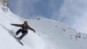 Ein Snowboarder f&auml;hrt eine steile, schneebedeckte Piste hinab und wirbelt Pulverschnee auf.
