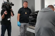 Mehrere Pakete Marihuana, die im Gepäck eines Verdächtigen gefunden wurden, werden auf einer Waage gewogen, um das Gesamtgewicht zu ermitteln, während ein Kameramann filmt.