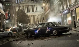 Die Attent&auml;ter haben die Stra&szlig;e zerst&ouml;rt und Autos durch die Luft fliegen lassen. Agent H (Chris Hemsworth) und Agent M (Tessa Thompson) haben mit ihren Waffen Deckung vor einem in der Stra&szlig;e liegenden Auto gesucht.