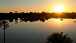 Die untergehende Sonne spiegelt sich auf der glatten Oberfl&auml;che eines Sees im Pantanal &ndash; ein magischer Moment.