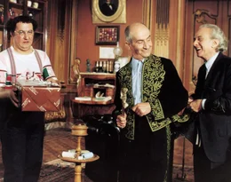 W&auml;hrend Charles (Louis de Fun&egrave;s, m.) mit seinem privaten Schneider (Marcel Dalio, r.) scherzt, versucht G&eacute;rard (Coluche, l.) seiner Angebeteten Marguerite mit einem Pr&auml;sent zu schmeicheln.